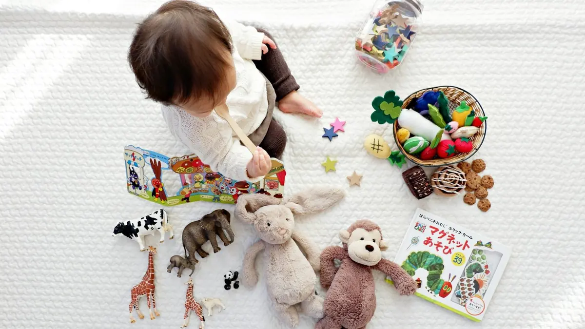 boy sitting on white cloth surrounded by toys