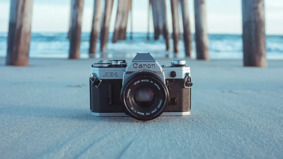 black and gray Canon AE-1 camera on gray sand under brown dock near body of water at daytime