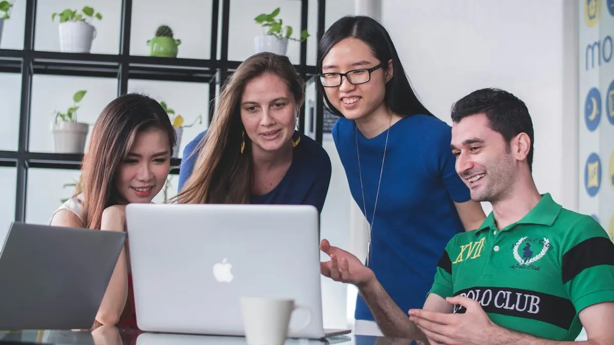 four people watching on white MacBook on top of glass-top table