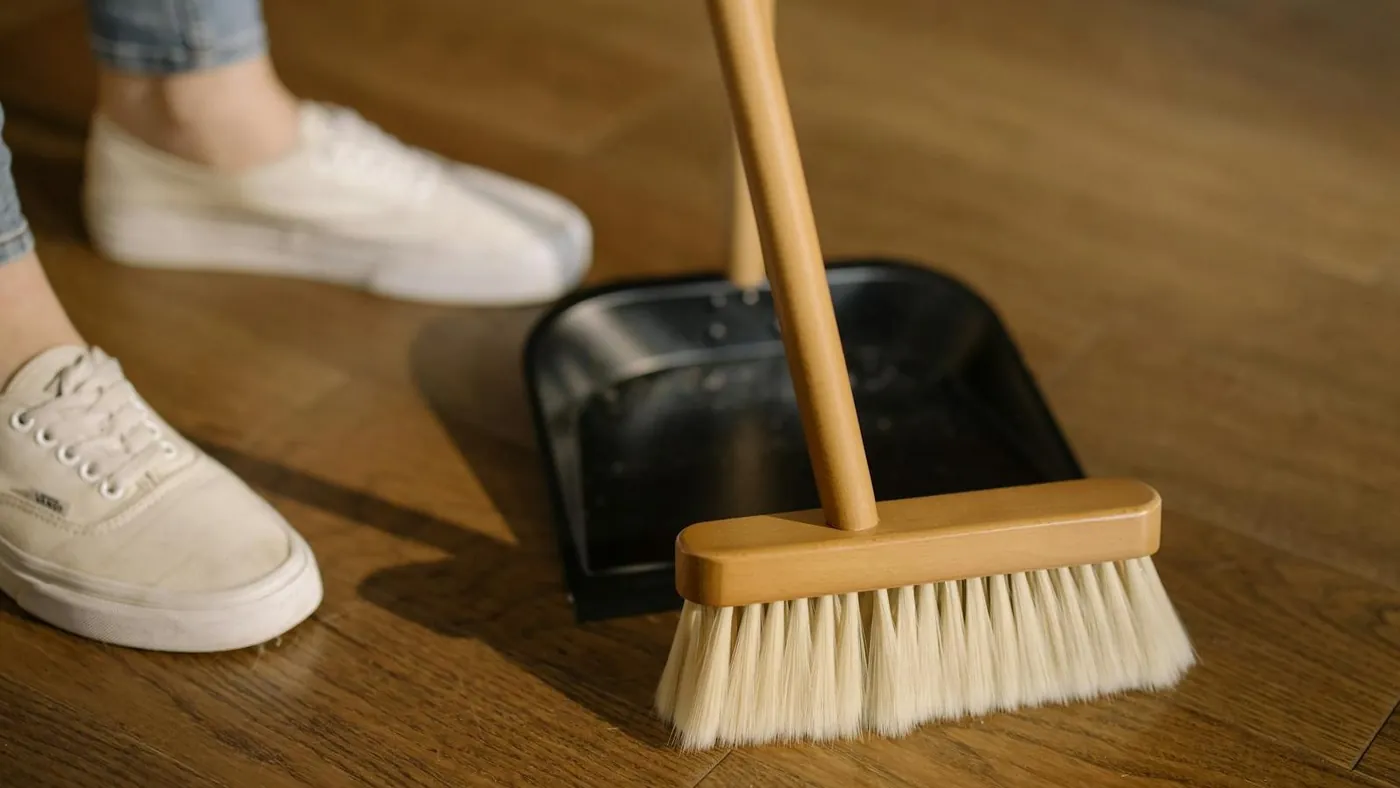 Person Wearing White Pants and White Socks Standing Beside Brown Broom
