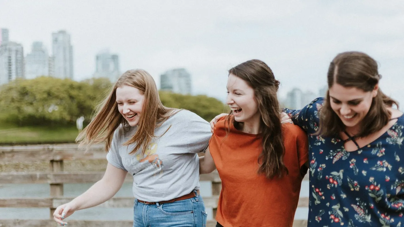 three women walking on brown wooden dock near high rise building during daytime